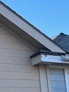 Tan siding, white trim, gray roof edge. Blue sky.