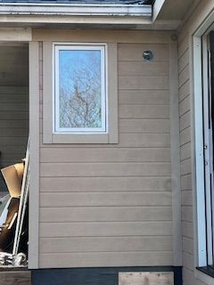 Beige siding on a house with a window framed in tan. A sliding glass door is on the right.