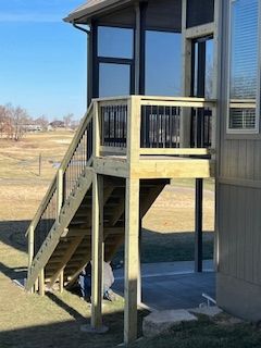 Wooden deck with stairs leading to a screened porch, against a house.