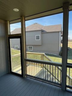 Screened-in porch with view of a house. Gray decking and railing. Black door. Sunny day.