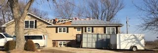 House with roof being repaired, van, and trailer outside on a sunny day.