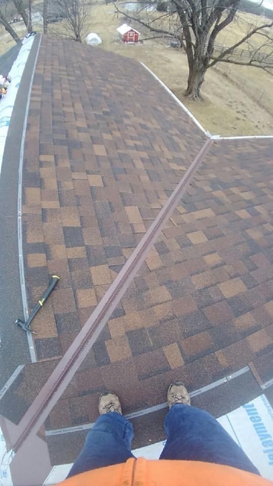 Person standing on a brown shingled roof, hammer nearby. Roofing work in progress.