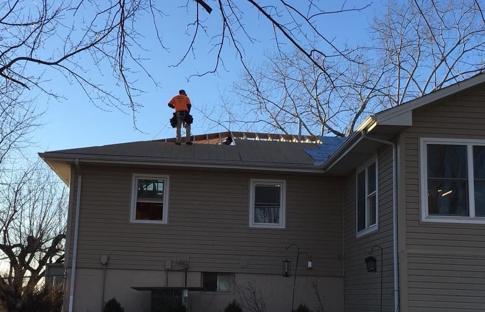 Roofer on a residential roof, repairing or installing roofing material. Tan siding, blue sky.
