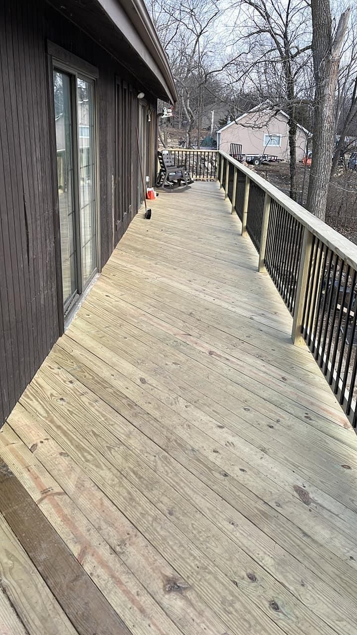 Wooden deck with decorative railing next to a house. Angled planks create a long, narrow surface.