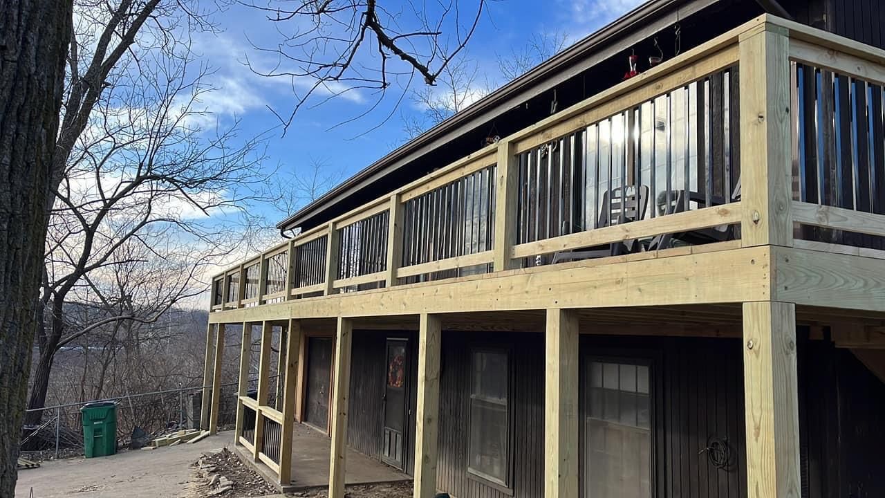 Wooden deck extension on a weathered building. Metal siding. Sunny day with a view of a hillside and sky.