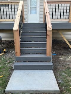 Concrete steps leading up to a deck with gray composite stairs, wooden posts, and a white door.