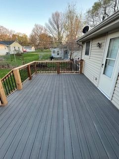 Gray composite deck attached to a house with a white door. Deck has wooden railings and overlooks a green lawn.