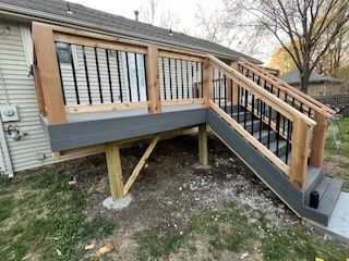 A wooden deck with stairs attached to a house. Gray decking and black railings.