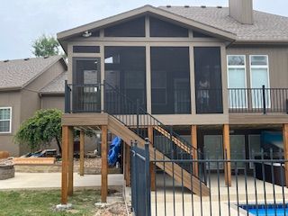 Screened porch and deck attached to a light brown house with black railings and stairs; a swimming pool is visible.