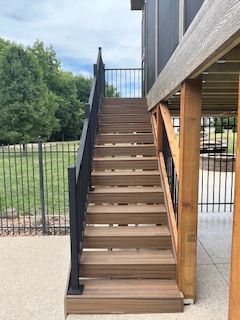 Outdoor staircase with brown steps and black railing leading up to a deck.