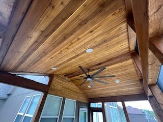 Wooden ceiling with recessed lights and a ceiling fan in an outdoor room.