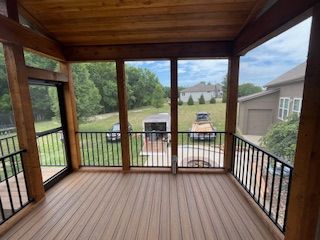Screened-in porch with wood ceiling and floor, black railings, and a view of a yard and houses.