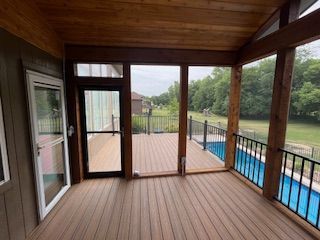 Wooden screened-in porch with door to house, decking, and view of a pool.