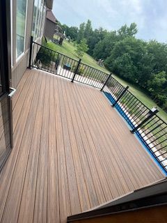 Wooden deck with black railing, overlooking a grassy hill and trees under a cloudy sky.