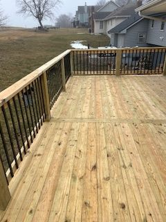 Wooden deck with black railings overlooking a grassy yard and houses.