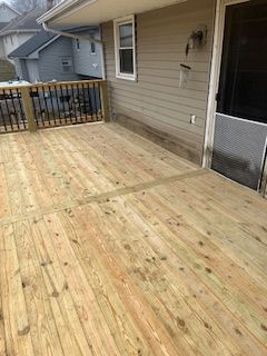 Wooden deck attached to a light brown house with black railing and screen door.