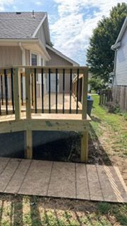 Wooden deck with black railings. A ramp leads to the deck. Adjacent is a grassy yard.
