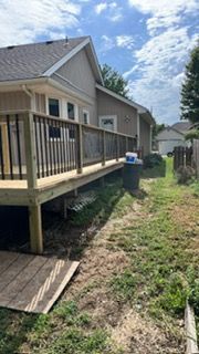 Wooden deck attached to a light brown house with dark railings and a pathway to a grassy yard.