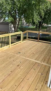 Wooden deck with black railings. Trees in the background. Bright, sunny day.