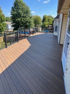 Composite deck with black railing and angled planks. A house is on the right, and a pool is in the background.
