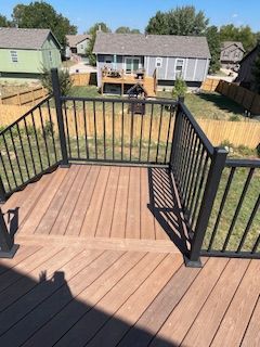 Brown deck with black railing overlooking a yard with houses.