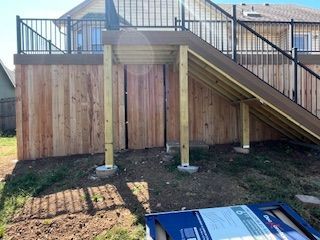Wooden deck with stairs, under-deck storage, and black railings; next to a house with a grass yard.