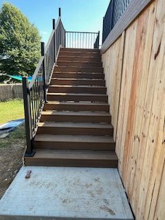 Wooden outdoor staircase with black railings, concrete base, and wooden siding.