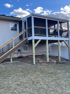Screened porch with stairs attached to a beige house, with wooden railing. Blue sky.