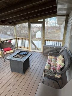 Screened-in porch with brown composite deck, wicker furniture, and a fire pit. Trees and a yard are visible outside.