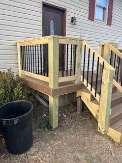 Wooden porch with black railings, brown steps, and black trash can in front of a white house.