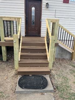 Wooden stairs leading to a brown door with black wrought iron railing and a welcome mat on the ground.