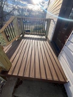 Wooden deck with railing attached to a house. Brown deck boards, sunlight.