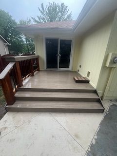 Brown composite deck with steps leading to sliding glass doors, on a light concrete patio.