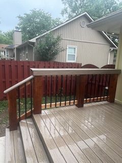 Wooden deck with brown and black railing, steps, and red fence behind.