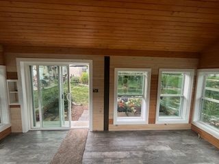 Sunroom interior with sliding glass door and windows; wood paneling, gray floor.