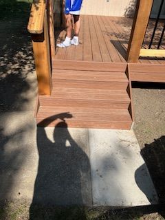 Wooden deck stairs leading to a deck, person standing on the deck, concrete patio below.