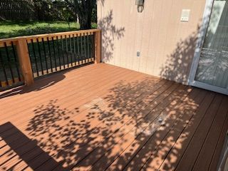 Wooden deck with black railing and light-colored siding, casting shadows from nearby tree.