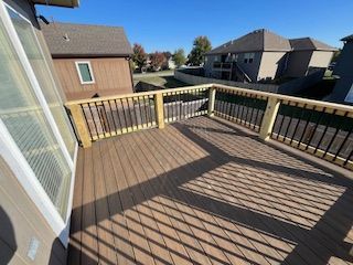 Wooden deck with black railing and composite decking, overlooking suburban homes under a blue sky.