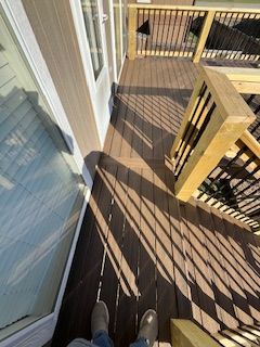 Brown deck with stairs, leading down from a white door. Shadows from the railing fall across the deck.