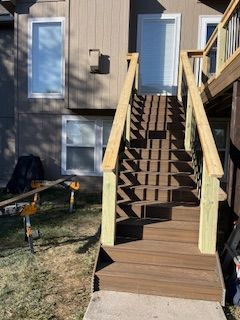 Brown wooden stairs with light yellow railings lead to a door on a tan house.