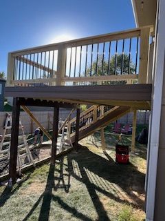 A partially built wooden deck with a railing and steps, in a backyard under a sunny sky.