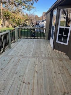 Wooden deck attached to a house with black railings and a white door, overlooking a yard.