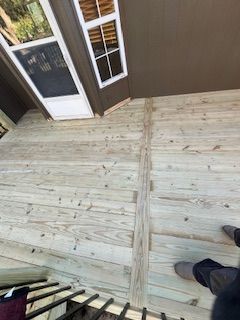 Wood deck with a brown trim and a white window. A person's feet are visible.