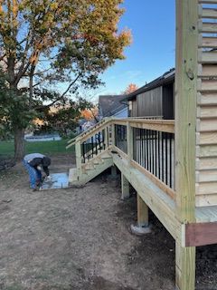 Construction worker working on deck stairs. Wooden deck with black railing. Outdoors, daytime.