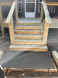Wooden outdoor stairs leading to a doorway, with a newly poured concrete landing.