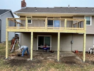 Wooden deck under construction attached to a house. A person works on the ground level.