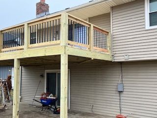 Wooden deck attached to a house with a person working; building materials and a sliding door are visible.