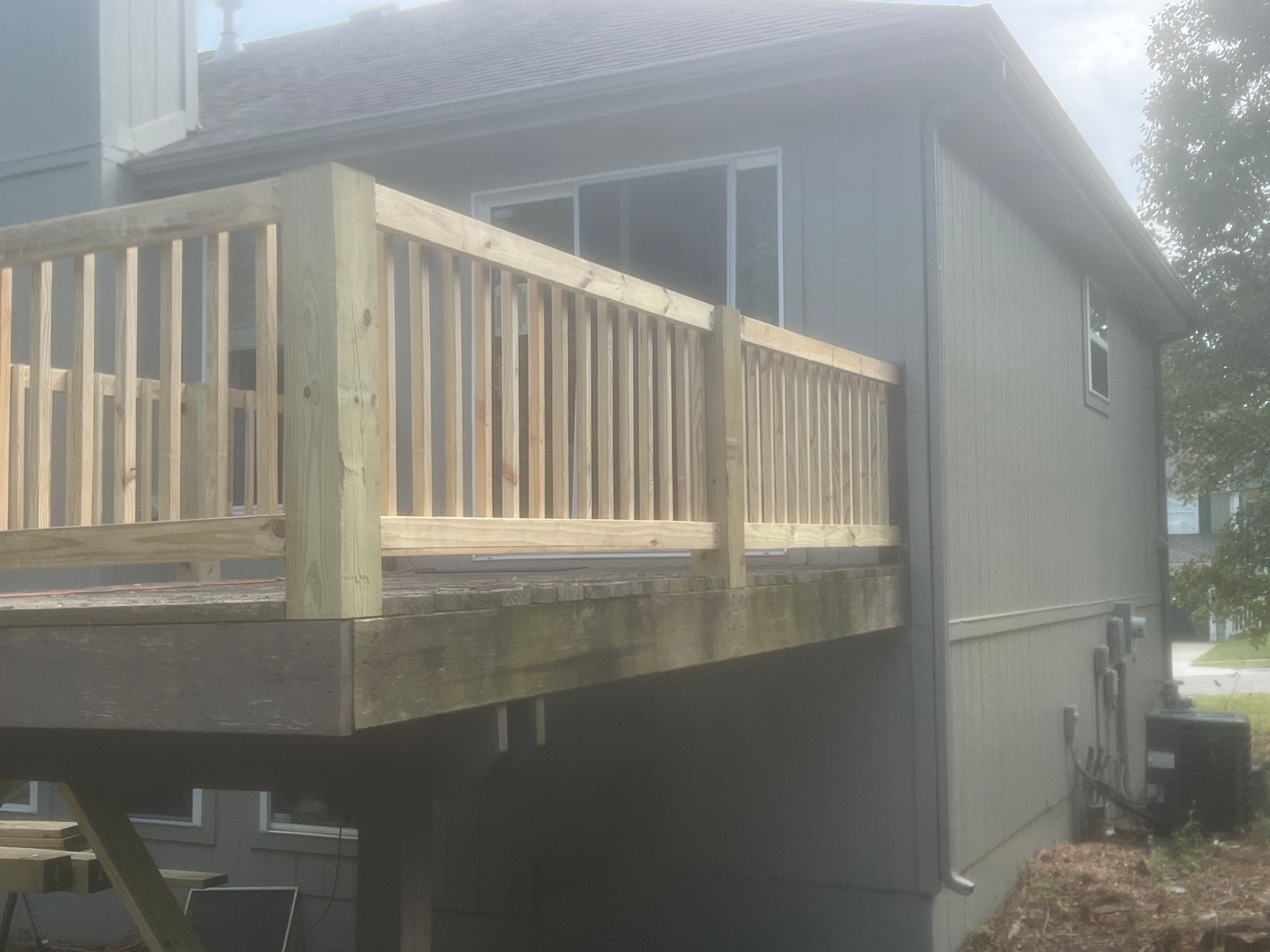 A wooden deck with a newly built railing is attached to a gray house.
