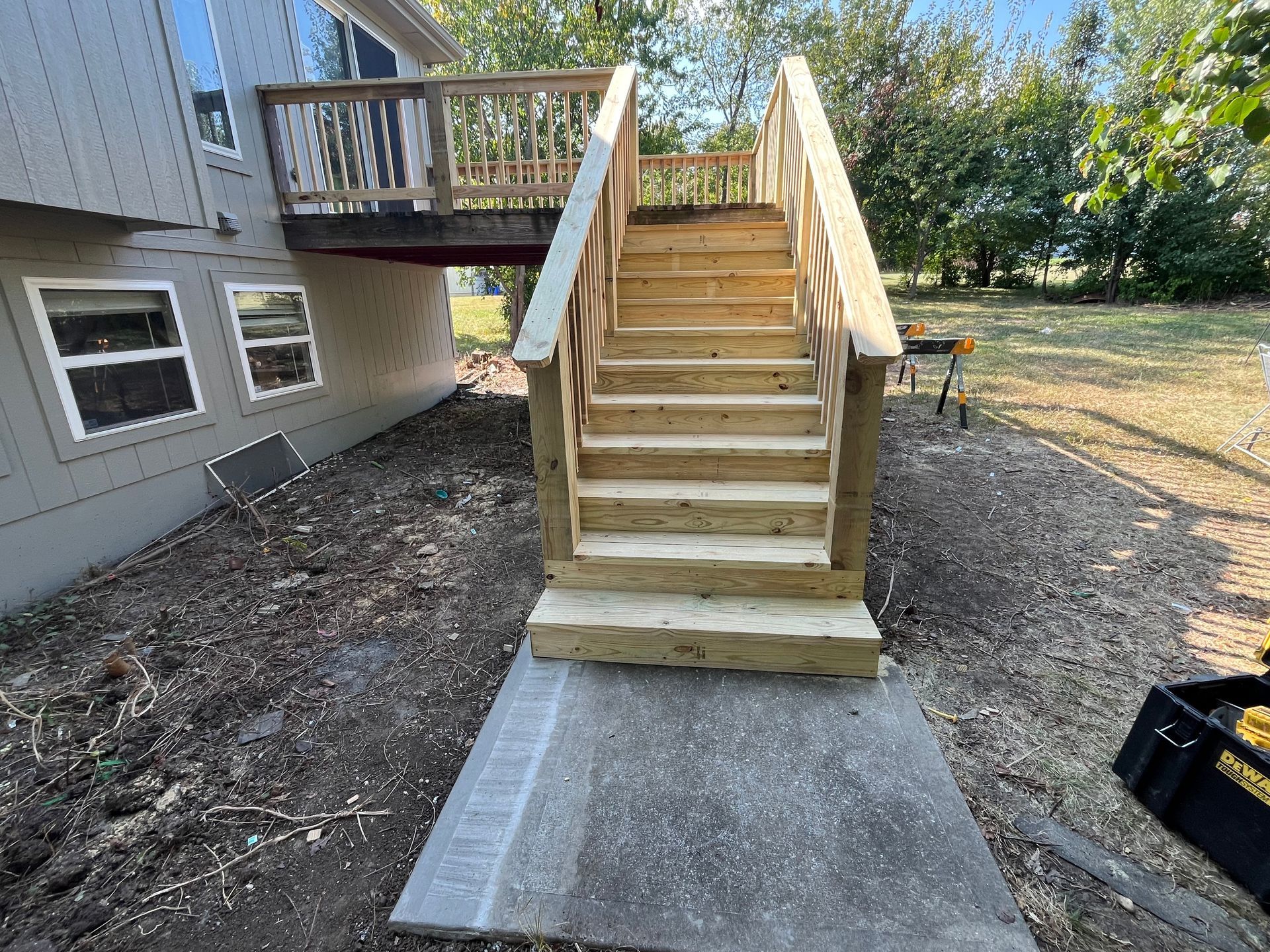 Wooden outdoor staircase leading from a deck to a concrete walkway.