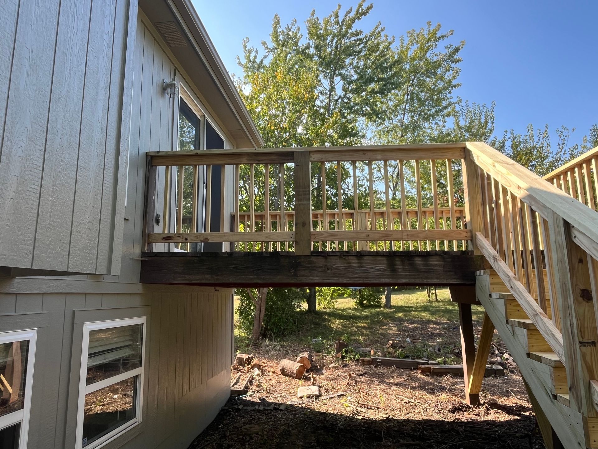 Wooden deck attached to a house with stairs leading down to a yard, on a sunny day.